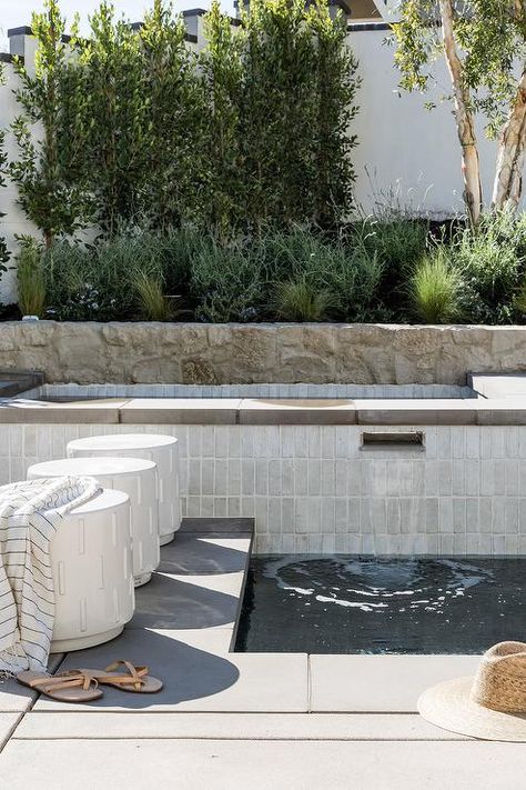 Spa features white stacked tiles and a pool waterfall. Backyard Idea On Hill, Daltile Pool Tile, Stucco Pool Wall, Precast Pool Coping, T Shaped Pool, Pure Salt Kitchen, Vertical Pool Tile, Backyard Pool Remodel, Zellige Pool Tile