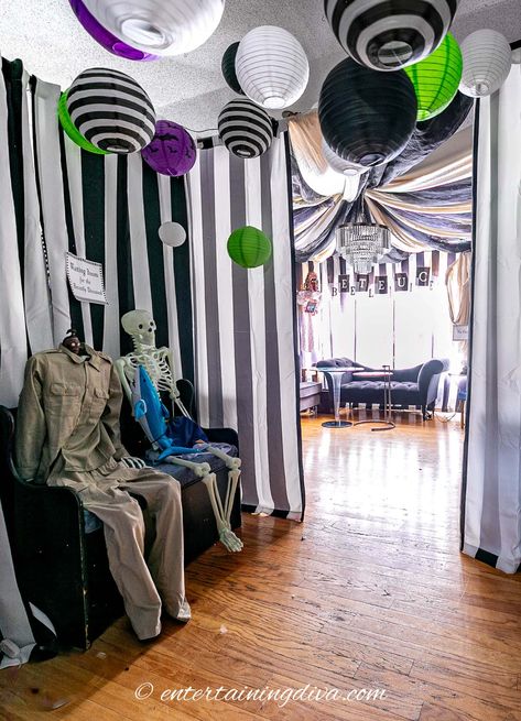 The Beetlejuice party waiting room decorated with black and white paper lanterns and skeletons dressed like shrunken head man and dead surfer Beetlejuice Theme Movie Night, Beetlejuice Watch Party, Beetle Juice Themed Halloween Party, Beetlejuice Office Decorations Diy, Beetlejuice Dining Room, Beetlejuice Party Decorations Diy, Diy Beetle Juice Decorations, Black And White Halloween Party Decor, Beetlejuice Skeleton