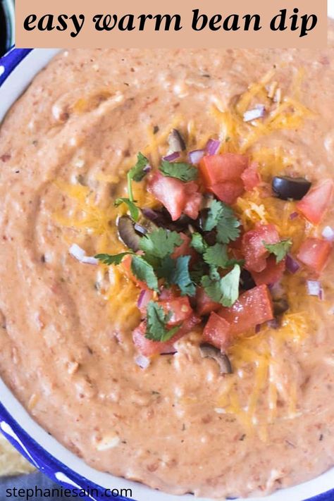 warm bean dip in a white and blue bowl topped with cheese, chopped tomato, chopped black olives, chopped red onion and cilantro Homemade Bean Dip, Hot Bean Dip, Cream Cheese Bean Dip, Mexican Bean Dip, Warm Bean Dip, Easy Bean Dip, Salsa Chili, Refried Bean Dip, Bean Dip Recipe