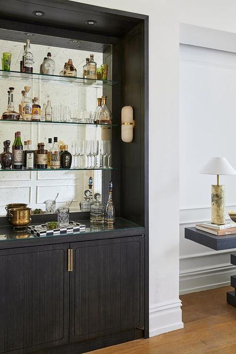 Black bar design features black cabinets with brass hardware and glass shelves on an antiqued mirror backsplash. Black Wet Bar, Antiqued Mirror Backsplash, Brownstone Living Room, Glass Bar Shelves, White Bar Cabinet, Black Bar Cabinet, Bar Nook, Home Wet Bar, Antiqued Mirror