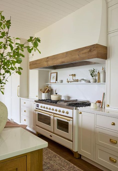 A brass swing arm pot filler is fixed to a marble slab backsplash between a white plaster hood with wood trim and a marble floating spice shelf, while white inset drawers with vintage brass knobs flank a white and gold French range. Hood With Wood Trim, French Range, White Cottage Kitchen, Blue Laundry Rooms, Oven Hood, Off White Kitchens, Shiplap Backsplash, Wood Range Hood, Marble Shelf