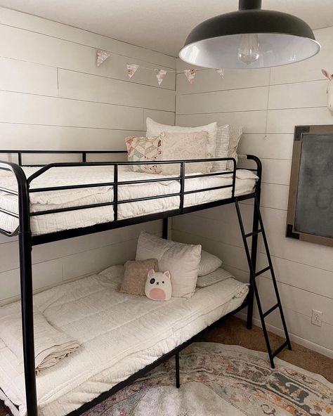 This vintage bedroom features a black metal bunk bed frame that contrasts against the white bedsheets. The white shiplap walls complement matching bedsheets and wooden floors. Lay a round vintage mat over the floor to add a visual focus. Low Ceilings Ideas, Bedroom With Black Bed Frame, Bedroom With Black Bed, Modern Retro Bedroom, White Coastal Bedroom, Bright Colored Furniture, White Bedsheets, Grey Striped Wallpaper, Bed On The Floor