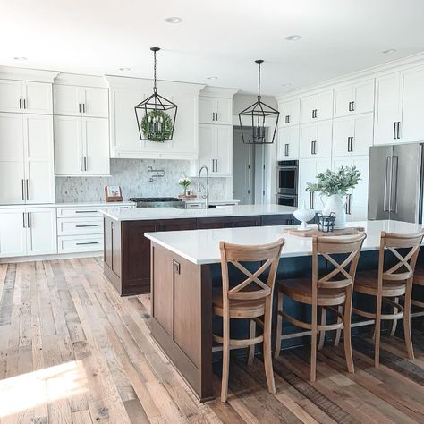 Two dark stained wood board and batten kitchen islands with white countertops are lined up in front of a kitchen with white shaker cabinets. The island with a breakfast bar is accessorized with wooden cross back bar stools. Board And Batten Kitchen, Wood Kitchen Design, White And Wood Kitchen, White Wood Kitchens, Double Island Kitchen, White Oak Kitchen, Dark Wood Kitchens, Wood Island, Wood Kitchen Island