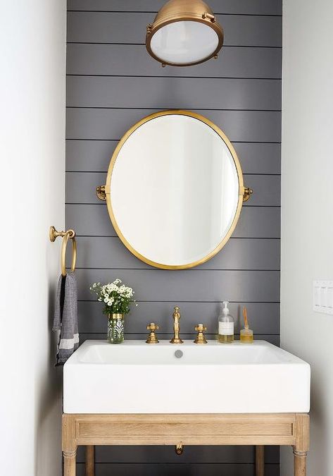 Small, stylish powder room boasts an oval brass pivot mirror mounted to a dark gray shiplap backsplash and matched with a brass industrial pendant. Shiplap Powder Room, Powder Room Storage, Powder Room Paint Colors, Shiplap Trim, Powder Room Tile, Powder Room Paint, Farmhouse Powder Room, Tiny Powder Rooms, Gray Shiplap