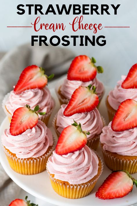 A plate of vanilla cupcakes with strawberry frosting and a sliced strawberry on top.