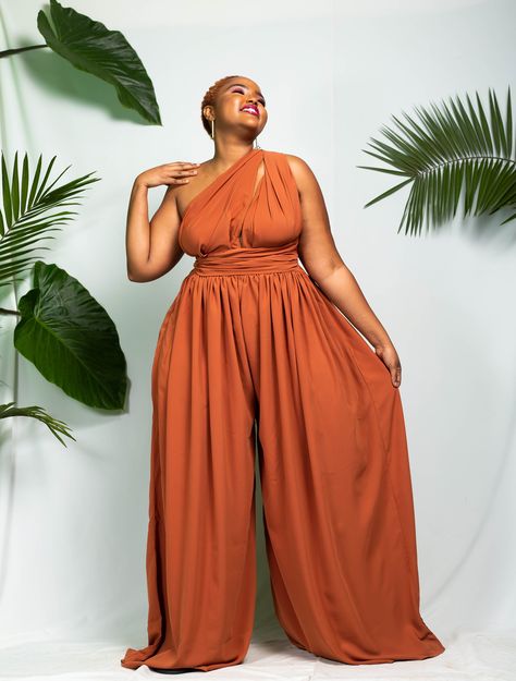 "The Yaounde Infinity Jumpsuit can be styled in multiple different ways as displayed in frame 1 and frame 2. It is made out of polyester fabric. It is perfect for summer & spring. It has pockets on both sides. Length: 64\" (163 cm) The length can be adjusted on request. The model is wearing a UK 16. It has an elastic waistband. CARE INSTRUCTIONS It can be machine-washed. Colour: Rust Orange SIZE GUIDE XXS/ UK 4 / US 0 = B -32 W -24 H -34 XS / UK 6 / US 2 = B -34 W -26 H - 36 S / UK 8 / US 4 Wedding Guest Jumpsuit Fall, Size Inclusive Fashion, Kenya Trip, Infinity Jumpsuit, Goddess Wear, Burnt Orange Jumpsuit, Wedding Attire For Women, Jumpsuit For Wedding Guest, Wide Leg Jumpsuits