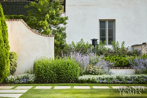 The outdoor area is framed by plantings, including English-style perennial borders set against the stucco and brick exterior. French Provincial Outdoor Area, Stucco And Brick Exterior, Perennial Borders, English Garden Design, Moorish Design, Harrison Design, Landscape Plants, Perennial Border, Brick Exterior