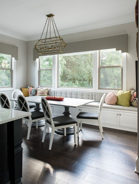 This beautiful breakfast nook came together with the white upholstered dining chairs and adorable grey window bench. The storage under the window seat is a great addition to this dining area. The throw pillows on the window seat add a pop of color and pattern and the large dining room light fixture centers the focus of the room. #colorfuldiningroom #colorfulthrowpillow #windowbench #diningwindowseat #africanpattern Dining Room Window Bench Seating, Bench Seating Under Window Dining Room, Banquette Seating Under Window, Dining Room With Window Bench, Bench Under Window Dining Room, Window Nook Dining Room, Dining Room Built In Bench Under Window, Bench Seating Kitchen Window, Bench Seats Under Windows