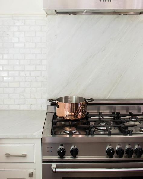 A two toned backsplash includes a white marble slab and white/gray subway tile that seemingly divides the counter space and the stainless steel cooktop stove. Modern Kitchen Stove, Kitchen Stove Design, Kitchen Design Details, White Marble Backsplash, Slab Backsplash, Stove Design, White Kitchen Cupboards, Kitchen Design Countertops, Kitchen Cooktop