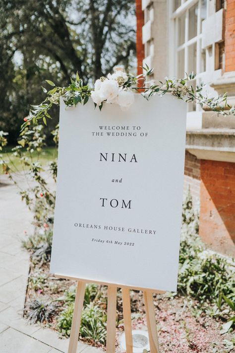 White wedding signage on wooden easel complete with floral decor Floral Easel Welcome Signs, Wooden Easel Wedding, Welcome Sign Easel Flowers, Welcome Wedding Sign Easel, Wedding Sign On Easel, White Wedding Signage, Welcome Signage Wedding, Wedding Sign Easel, Midi Bridesmaid Dresses