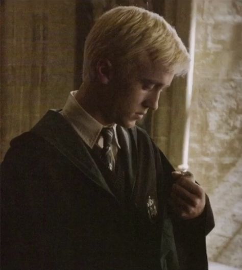 a rare photo of draco malfoy/tom felton (young) in 3rd-5th year is shown. draco appears to be looking down at this hands while in a slytherin robe. this dark academia aesthetic-like photo is based off the film, harry potter, at hogwarts to be precise. Tom Felton Young, Tom Felton, Dark Academia Aesthetic, Academia Aesthetic, Draco Malfoy, Dark Academia, Harry Potter, Blonde