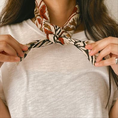 Close up of model tying a bandana around the neck. Ways To Fold Bandanas, Bandana With Outfit, Wearing A Bandana Around Neck, How To Tie Handkerchief Around Neck, How To Style Bandana Around Neck, Neck Scarf Tie, Neck Kerchief Outfit, How To Tie Neck Bandana, How To Tie A Western Scarf