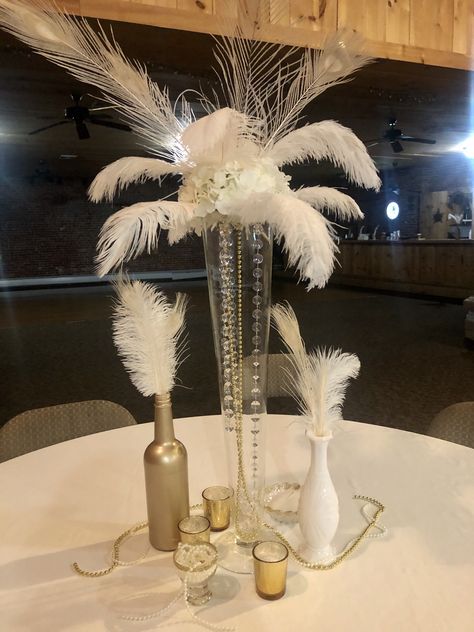 Roaring 20s decor with bleached peacock feathers, ostrich feathers, Hydrangeas Feather Centerpieces For Party, Small Feather Centerpieces Simple, Feather Table Decor, Black Feather Table Centerpieces, Feather And Pearl Centerpieces, Elegant Wedding Reception Tables With Feather Centerpieces, Flower Ball Centerpiece With Feathers, Vase With Feathers, Feather Boa Centerpiece