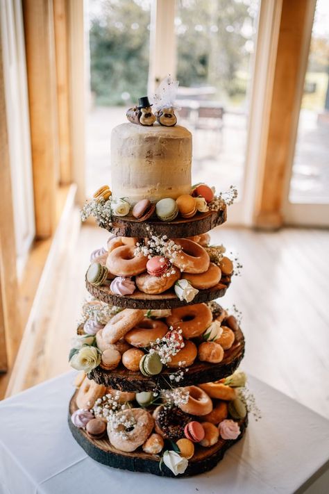 Log slice cake stand holding donuts, macaroons, flowers and a one tier cake on the top with colin the caterpillar bride and groom wedding cake toppers Log Slice Cake Stand, Alternative Wedding Cake Ideas, Doughnut Wedding Cake, Macaroon Wedding Cakes, Donut Wedding Cake, 3 Course Meal, Three Tier Wedding Cake, Colin The Caterpillar, Alternative Wedding Cakes