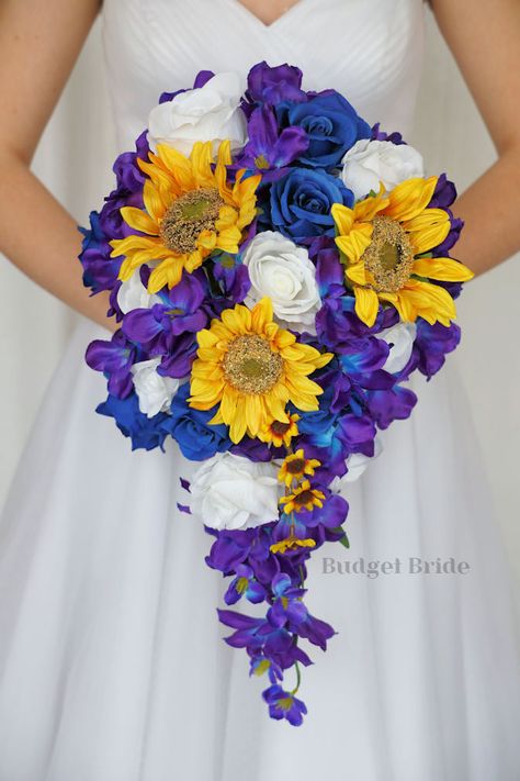 This lovely assortment of royal blue and white roses and sunflowers is bound to turn heads on your wedding day. This lovely cascading brides’ bouquet from the is an absolutely breathtaking arrangement for any bride to be, in any season. Bright greenery and galaxy orchids complete the look and add a delicate realism to this beautiful bouquet. This bouquet is 10” wide, 18” long, and is crafted by our in-house florists without using a foam base to anchor the flowers to the bouquet. Instead, we wire Cascading Sunflower Bridal Bouquet, Royal Blue And Yellow Wedding, Bouquet With Sunflowers, Royal Purple Wedding, Roses And Sunflowers, Small Bridesmaid Bouquets, Fake Wedding Flowers, Blue And White Roses, Fresh Wedding Flowers