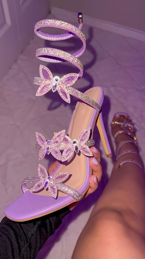 The Serena Butterfly Heel in a beautiful lilac color is both elegant and eye-catching. Adorned with butterfly rhinestone heels and a wrap around detail, this shoe is perfect for adding a touch of glamour to any outfit. With its unique design, it's sure to make a statement at any event. Butterfly Rhinestone Details Adjustable Coil Strap Lightly Padded Insole Heel Height Approximately 4” Runs .5 Smaller Thank You For Shopping At Berenis!! Butterfly Heels Purple, Rapunzel Shoes Heels, Purple And Silver Heels, Cute Heels Outfits, Quince High Heels, Black And Purple Heels, Purple Butterfly Theme Quinceanera, Silver Butterfly Heels, Homecoming Heels Silver