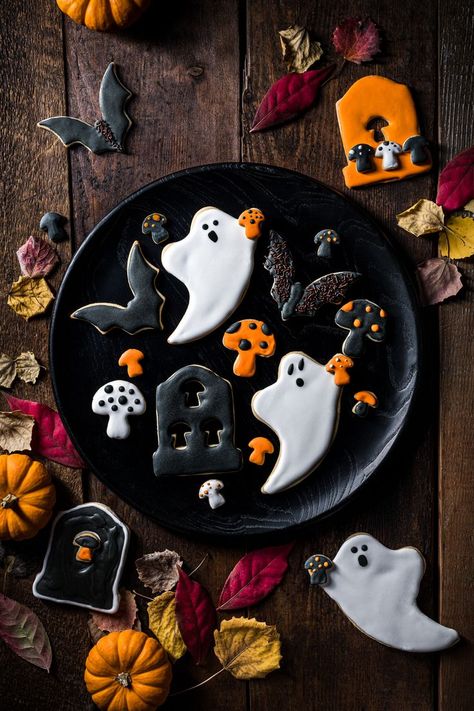 A series of Halloween cookies in the shape of ghosts, bats, tombstones and mushrooms decorated with white, orange and black royal icing placed on a black round serving board on a wood table Cookie Food Photography, Cookies Photography, Food Portrait, Sugar Cookies With Royal Icing, Mushroom Cookies, Cookies With Royal Icing, Halloween Sugar Cookies, Dark And Moody, Spooktacular Halloween