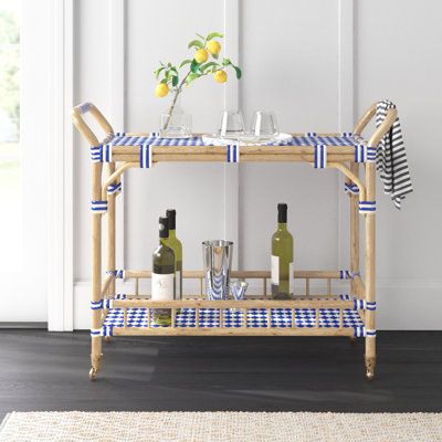 This bar cart offers a stylish way to serve up drinks and snacks, whether you're hosting a gathering or enjoying a relaxing evening at home. The solid bamboo frame features a light brown finish, while the top and bottom shelves showcase woven blue-and-white acrylic detailing for a coastal vibe in your space. With four wheels and two handles, this cart is easy to move around, and the included towel bar ensures you always have a cloth handy for spills. The cart's 50 lbs. weight capacity allows for Bar Cart Wood, Bar Corner, Wood Bar Cart, Relaxing Evening, Serving Cart, The Company Store, Florida House, Bar Art, Bamboo Frame