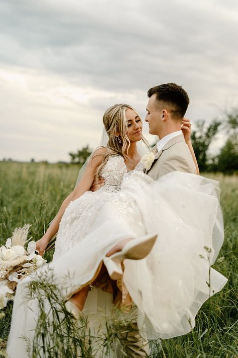 Nebraska based wedding photographer captures dreamy photos of a bride and groom in a field in Nebraska showing the bride in a beautiful white lace dress with floral details and a long veil and the groom in a tan suit while they walk through the field and he carries her.    #nebraskaweddingphotographer #brideandgroomportraits #romanticcoupleposes #coupleposingideas #weddingposes #weddingportraits