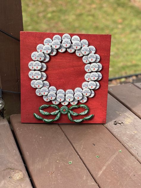 "This beautiful stained red poplar with a unique bottle cap design will really help change up your Christmas decor! Michelob Ultras are used for the white wreath and Heineken finishes the piece with a green bow. This is a great piece for any space during the holidays and the colors really catch the eye!  This piece is 11 1/2 \" x 11 1/2\" and about 1 1/2\" deep." Beer Cap Projects, Bottle Cap Design, Beer Bottle Cap Art, Bottle Top Art, Beer Bottle Cap Crafts, Plastic Bottle Tops, Bottle Top Crafts, Bottle Cap Projects, Soda Can Crafts