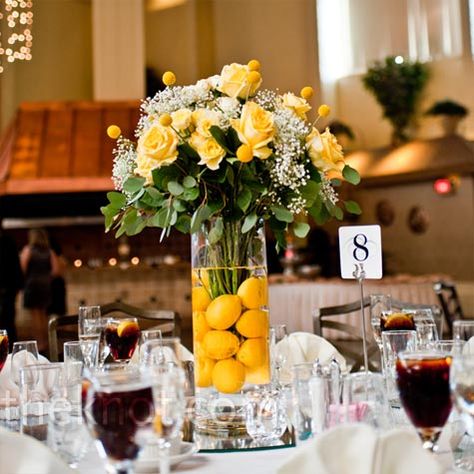 For the head table, the couple opted for a tall vase filled with submerged lemons and topped with an arrangement of roses. Lemon Centerpiece Wedding, Breakfast Italy, Lemon Themed Wedding, Lemon Centerpieces, Lemon Themed Bridal Shower, Citrus Wedding, Lemonade Party, Lemon Decor, Tall Vase