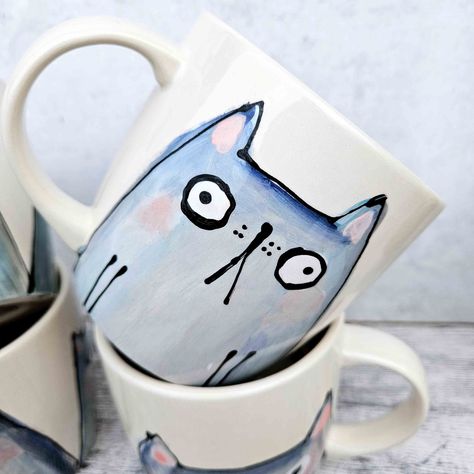 This listing is for one on my hand painted blue/grey cat mugs. Painted by hand, by me. Each mug is entirely unique. Once painted, it's then fired in the kiln, before being glazed and fired in the kiln again. This mug is hand painted and hand glazed so may contain small marks or imperfections making it totally unique. It is dishwasher and microwave safe, although I would recommend handwashing. Mug size is: 10.1cm D x 9.5 cm Height, holding 12oz of liquid (which is a big, but not *too* big cup of Christmas Pottery Mug Ideas, Painting On Cups Mugs, Paint A Mug Ideas, Mugs Painting Ideas, Hand Painted Pottery Mugs, Cat Pottery Painting, Pottery Painting Mug Ideas, Mug Painting Ideas Easy, Rainbow Ceramics