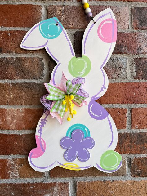 This door hanger is hand cut from MDF, painted with acrylic paint, then sealed for use indoors or outdoors. The sealant makes the item weather resistant NOT weather proof. Hangers will last longer when hung on a porch or under an over hang. This cute bunny can be hung on an entry door , a wall , your fireplace or anywhere else you need a little Easter fun!  Door hangers are individually hand painted so slight variations in color shown in photo may occur. Please ask any and all questions before purchasing. Custom orders may not be returned. If it is our mistake we will do our very best to rectify the situation.  Free shipping.  We do not ship outside of the US. Wooden Bunny Door Hanger, Easter Bunny Wood Crafts, Easter Wooden Door Hangers, Easter Door Hanger Wooden, Easter Door Signs, Painting Bunnies, Easter Door Hangers, Easter Cutouts, Fun Easter Crafts For Kids