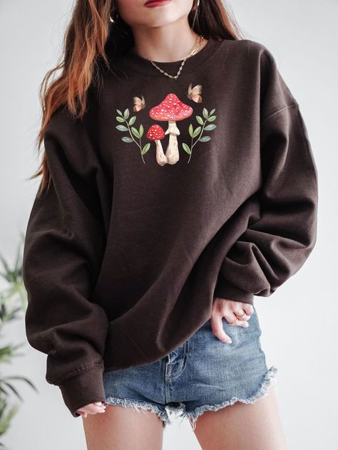 Enjoy the Cottagecore Aesthetic with this cute Mushroom Sweatshirt! This Cottage Core Mushroom Sweater is super comfy! Size up for a Trendy Oversized Look! Makes the perfect gift for that special Mushroom Lover in your life! ♥ Hello and Welcome to Meaningful Tees Shop! ♥ Printed on the most popular Unisex Sweatshirt, the Gildan 18000 is 50% Cotton / 50% Poly. The soft fleece lining makes it super Comfy and is sure to become your new favorite! ♥ All of our items are made one at a time with care for each customer : ) ♥ Please allow 3-7 BUSINESS days (usually 4-5) for your item to be created PLUS shipping time via USPS ♥ This Unisex Sweatshirt fits like a Men's on Women, but is not overly large. ♥ For a RELAXED FIT, your usual size will typically work, but please consult the Size Chart in the Mushroom Embroidery Sweater, Cottage Core T Shirt, Cottage Core Trousers, Mushroom Outfit Aesthetic, Mushroom Aesthetic Outfit, Nature Clothes Aesthetic, Spring Cottagecore Outfits, Mushroom Core Aesthetic, Cute Shirts Aesthetic