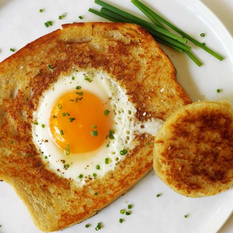 An overhead shot of Eggs in a Basket on a white plate with chives sprinkled on top and some laying the side of the plate. Egg In A Basket, Eggs In A Basket, Breakfast Sausage Recipes, Toad In The Hole, How To Make Eggs, Chewy Peanut Butter Cookies, Breakfast Ingredients, Smothered Chicken, Layered Salad