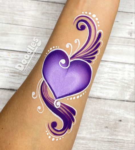 Colorful face and body painting design that was created with a purple one stroke cake. It is adorned with deep purple swirls. One stroke hearts are easy to create. Follow this one stroke tutorial in our face painting tutorial on YouTube! Face Painting On Hand, Hand Face Paint, Descendants Face Paint, Valentines Face Painting Ideas, Heart Face Paint, Purple Face Paint Ideas, Face Painting Heart, Purple Face Paint, Face Paint On Arm