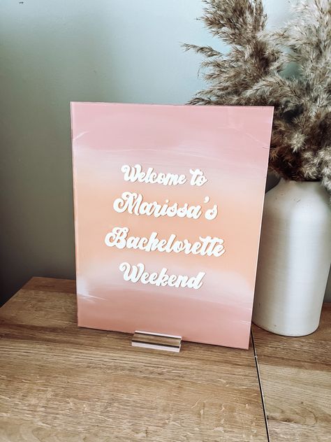 Acrylic sign painted with pink and coral in an ombré effect to look like a sunset with the words “welcome to Marissa’s bachelorette party” in a white hand lettered retro font Boho Beach Bachelorette, Bachelorette Signage, Bachelorette Party Sign, Rose Gold Background, Bachelorette Party Signs, Bachelorette Signs, Acrylic Welcome Sign, Bachelorette Party Beach, Bachelorette Party Planning