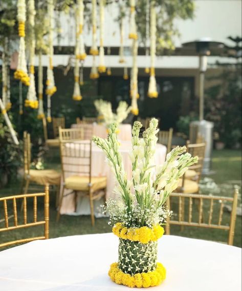 Elegant & minimal traditional table decor with genda flowers, mogra & baby’s breath | Outdoor day mehendi decor | leaf and flower vase | Decor by Grafico events | #indianwedding  #decorideas  #decorinspiration  #traditionaldecor #indianweddingdecorations  #decoration #mehendidecor  #ikebana  #weddingdecorations #yellowdecor #floraldecor #wittyvows #centerpieces  #tablestyling Small Wedding Table Decorations, Traditional Table Decor, Flower Vase Decor, Yellow Centerpieces, Minimal Traditional, Mehendi Decor, Flower Garland Wedding, Intimate Wedding Reception, Mandap Decor