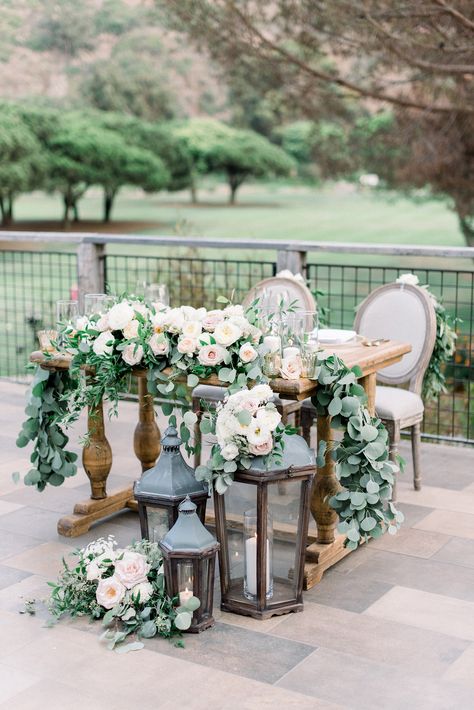 Sweetheart table with garland and lanterns, rustic wedding at the ranch Laguna Beach Cheap Wedding Table Centerpieces, Sweetheart Table Flowers, Head Table Wedding Decorations, Wedding Sweetheart Table, Bride Groom Table, Beach Wedding Tables, Wedding Candles Table, Rustic Beach Wedding, Sweetheart Table Decor