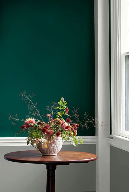 A hunter green wall with white trim and gray wainscoting frames a round wooden table on which a vase of flowers sits. Emerald Green Mudroom, Jewel Toned Green Paint, Jewel Tone Green Bedroom, Jewel Tone Entryway, Terry Town Green Benjamin Moore, Emerald Green Painted Walls, Two Tone Green Wall, Jewel Green Paint Colors, Hunter Green Benjamin Moore