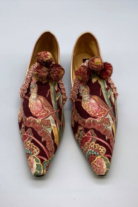 A pair of striking pointed toe flat shoes are photographed from above against a pale grey background. The antique French printed textile has a design of an exotic long tailed bird perched on a branch amongst foliage and flowers. Tones of teal, pinks and golds against an aubergine ground. The high fronts are edged with silk braid and embellished with multi-coloured silk pompom tassels. Aubergine Dress, Bird Shoes, Wearable Art Fashion, Brighton England, Feminine Shoes, Embellished Shoes, Stunning Shoes, Antique Textiles, Historical Costume