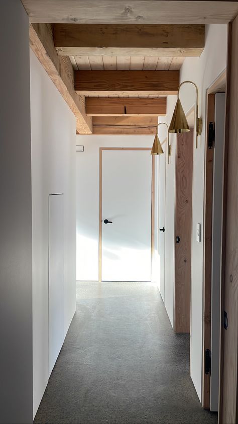 No trim here. This modern hallway features exposed timbers and door frames, flush doors with shadow gap reveals and a polished concrete floor. To top it off, handmade brass sconces amp up the cozy evening vibes. Concrete Floor Hallway, Modern Timber Frame, Hallway Sconces, Polished Concrete Floor, Contemporary Hallway, Shadow Gap, White Hallway, Hallway Door, Evening Vibes