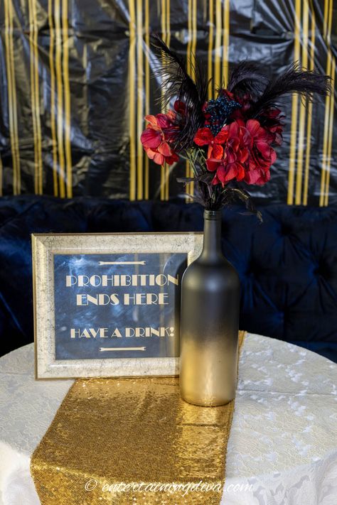 "Prohibition ends here, have a drink" sign on a table with a wine bottle vase Roaring 1920s Party, 20s Party Theme, 20s Theme Party, Wine Bottle Vase, Decades Party, Gatsby Birthday Party, Ostrich Feather Centerpieces, Gatsby Party Decorations, Great Gatsby Themed Party