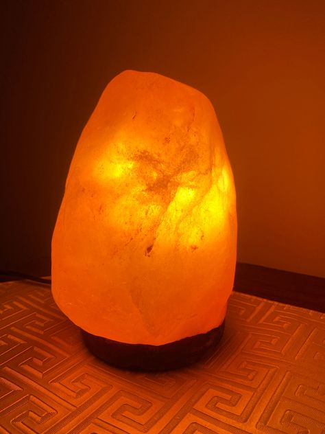 A Himalayan salt lamp is a decorative piece crafted from pink salt crystals mined from the Himalayan Mountains. It usually stands on a sturdy Neem wooden base, adding to its natural and rustic appeal. These lamps vary in size and shape, with some appearing more rough-hewn and others carved into smoother, more geometric forms.  Dimensions: As this is a natural rock the size and lighting vary in each lamp. Every lamp is different from the other. The pink salt crystals have a warm, inviting color, ranging from soft pink to deeper orange hues, depending on the thickness and mineral content of the salt. When lit from within by a small bulb, the lamp emits a soft, ambient glow that creates a calming and cozy atmosphere. This gentle illumination is not only soothing to the eyes but is also said t Cozy Table Lamps, Salt Lamp Aesthetic, Warm Lamps, Salt Lamp Decor, Warm Light Lamp, Cozy Lamp, Rock Lamps, Realistic Wishlist, Rock Salt Lamp