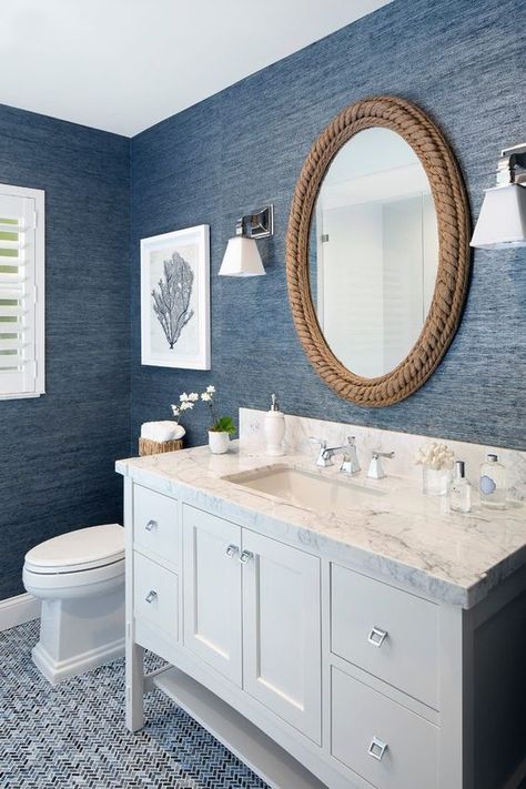 a nautical bathroom with blue grasscloth wallpaper, a neutral vanity, a mirror covered with rope, some sea inspired decor and white appliances Wallpaper Cottage, Coastal Style Bathroom, Canadian Decor, Makeover Kamar Mandi, Coastal Bathroom Design, Styl Hampton, Beach House Bathroom, Rope Mirror, Cottage Decorating