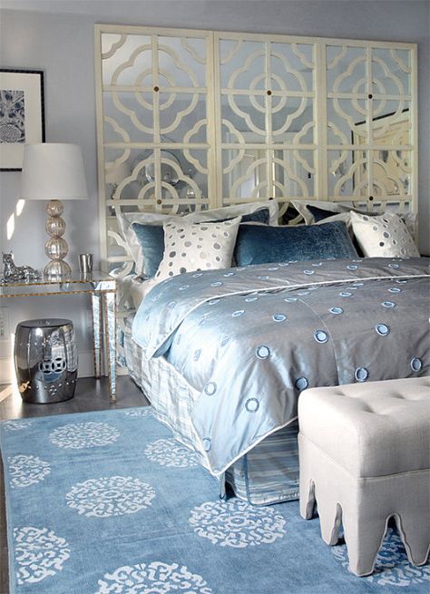 Glam bedroom with gray blue walls paint color, mirrored console table nightstands with gold trim, ivory mirrored quatrefoil pattern floor screen used as headboard, champagne metal lamps, silver garden stools, Madeline Weinrib Atelier Light Blue Mandala Rug and light gray linen tufted ottomans. Blue Gray Bedroom, Blue And White Decor, Blue Painted Walls, Silver Bedroom, Mirror Headboard, Contemporary Nightstand, Glam Bedroom, Mirrored Console Table, Mirrored Nightstand