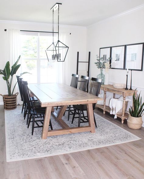 Light wood dining table is accented with black spindle back dining chairs under a black linear lantern light. Gray and beige vintage area rug for kitchen table is laid underneath the table covering stained wood flooring. Dining Table With Grey Floor, Light Table Dark Chairs Dining Room, Light Wood Dinning Table Black Chairs, Dining Table With Black Spindle Chairs, Light Gray Rug Living Room, Rug Under Dining Table Or Not, Grey Wash Dining Table With Black Chairs, Light Wood Flooring Dining Room, Light Farmhouse Dining Table