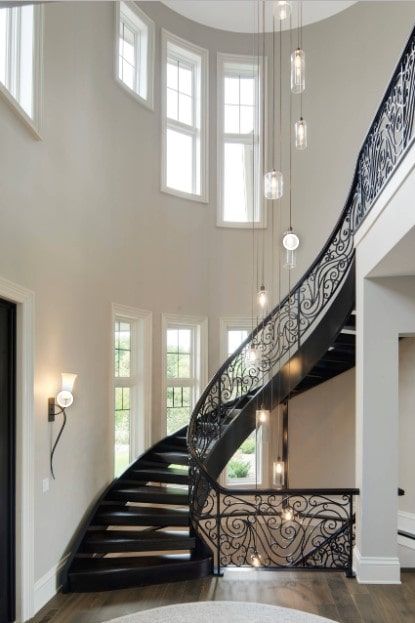 Black wooden staircase styled with an ornate balustrade and illuminated by a wall sconce and industrial chandelier. Staircase Frames, Metal Staircase, Transitional Staircase, Staircase Styles, Wood Handrail, Relaxing Home, Wood Staircase, Recessed Ceiling Lights, Staircase Lighting