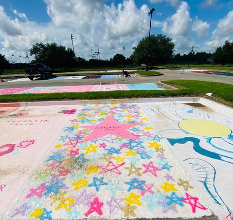 White parking spot with multicolored stars all over with large pink star in the middle with lettering in black on it Iconic Senior Parking Spots, Cute Parking Spot Paintings, Parking Spot Painting Junior Year, High School Painted Parking Spots, Painted Parking Spots, Highschool Parking Spot Ideas, Painted Parking Spots Senior Girls, Chalking Senior Parking Spots, Painted Parking Spaces Ideas