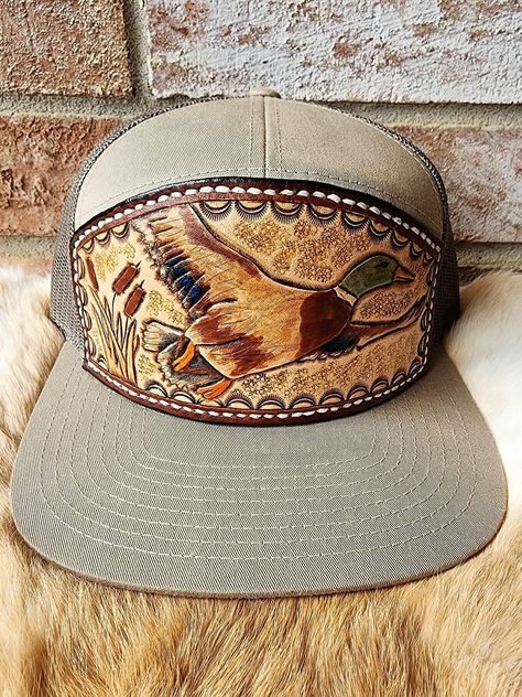 This is a custom tooled leather handmade mat. It is of a Mallard taking flight. This is a great accessory to get for the Duck Hunter and or individual who enjoys birds!  This is a 7 Panel trucker hat made by Richardson that is Pale Khaki and Loden Green. It is a snapback enclosure style.  If you have any desire to create your own front of a hat send me a message and I will certainly work with you to make your ideas become tangible! Thank you for the consideration of my work! 7 Panel Hat, Custom Leather Work, Loden Green, Country Hats, Custom Trucker Hats, Cowboy Wedding, Duck Hunter, Cowgirl Aesthetic, Custom Belt