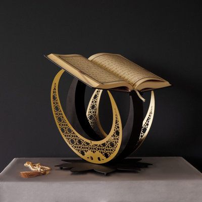 This Metal Hilal Qur'an Stand is the perfect piece of Islamic decor for any Muslim home. Crafted from strong and durable metal, its perfect design is beautiful to look at and easy to use. It both serves as a Quran Holder and stunning Islamic decor, providing a decorative and meaningful accent to any space. Also, great gift for your friends. Everly Quinn Color: Black/Gold | Everly Quinn Metal Hilal Qur'an Stand w / Qur'an in Black / Gold | 13" H X 12.5" W X 12.5" D | Wayfair | Home Decor Quran Stand, Trophy Stand, Aesthetic Islamic, Prototype 2, Prayer Room Ideas, Arabic Decor, Ramadan Decor, Gifts Book, Ramadan Decoration