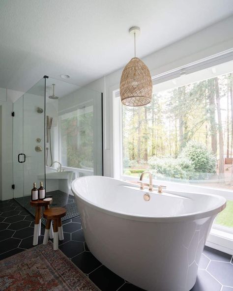 White freestanding bathtub is placed in front of a large window beneath modern bathroom pendant lighting. Black tile covers the floor of the bathroom joined by a vintage patterned rug. Shower with glass enclosure completes this space. Pendant Lighting Over Bathtub, Bathroom Pendant Lighting Over Tub, Pendant Light Over Bathtub, Light Over Bathtub, Pendant Lighting Black, White Shiplap Wall, Blue Ceilings, White Bathroom Tiles, Grey Countertops