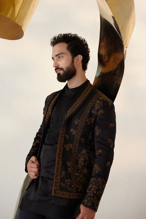 Black & Gold Short Jacket | Jatin Malik Presenting our striking all-black short jacket set, elevated with exquisite gold zari work and a distinguished shawl collar lapel detail. This ensemble exudes sophistication and modernity, making a bold statement with its sleek design and attention to detail. Paired with a short-length tone-on-tone kurta and tapered trousers, it offers a harmonious balance of style and versatility. Whether it's a formal occasion or a stylish gathering, this ensemble is sure to command attention and leave a lasting impression with its timeless elegance and impeccable craftsmanship. Included in purchase: Short Jacket, Kurta, Trousers Product Specification Color: Black Fabric: Linen Silk Occasion: Engagement, Wedding, Bridal, Reception Style: Short Jacket, Kurta, Trouse Jatin Malik, Wedding Kurta For Men, Blouse Yoke, Cute Celebrity Couples, Gold Shorts, Indian Groom, Haldi Ceremony, Fashion Suits For Men, Tapered Trousers