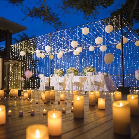 Turn your wedding into a dreamy affair by setting up celestial decorations. Magically light up the space by arranging plenty of led pillar and tealight candles. Cast a magical spell on your guests by setting up a wistful wedding tablescape with starry effect using curtain string lights and hanging paper lanterns. Dress up the table in a white tablecloth and arrange chic place setting along with white floral centerpieces. Style the chairs in white sashes and make your guests feel truly special. Outdoor Wedding Decor, Lantern With Fairy Lights, Party Decorations Table, White Paper Lanterns, Wedding Ambiance, Hanging Paper Lanterns, Whimsical Wedding Decorations, Led Curtain Lights, Outdoor Dinner Parties