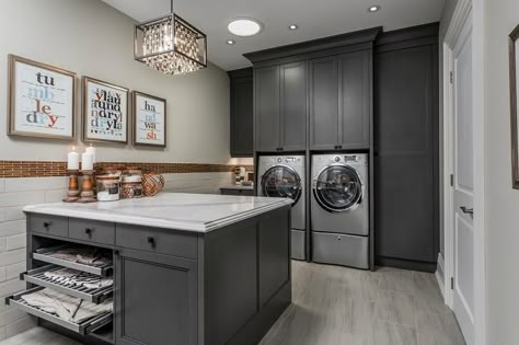 Charming gray laundry room boasts a gray front loading washer and dryer enclosed beneath and between dark gray cabinets accented with matte black hardware. Laundry Room Island, Laundry Room Countertop, Grey Laundry Rooms, Laundry Room Storage Shelves, Stylish Laundry Room, Room Storage Diy, Basement Laundry Room, Dream Laundry Room, Basement Laundry