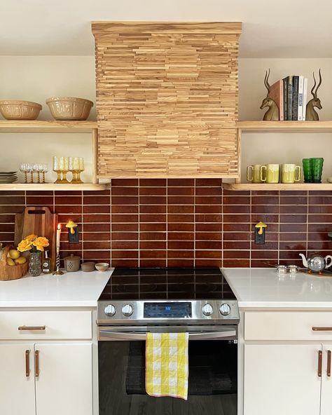 White kitchen with deep red brown tile backsplash, wooden shelves, and decorative stove hood Red Backsplash Kitchen, Red Tile Kitchen, Brown Tile Backsplash, Brown Kitchen Tiles, Kitchen 80s, Red Kitchen Tiles, 80s Kitchen, Red Backsplash, Kitchen Cost